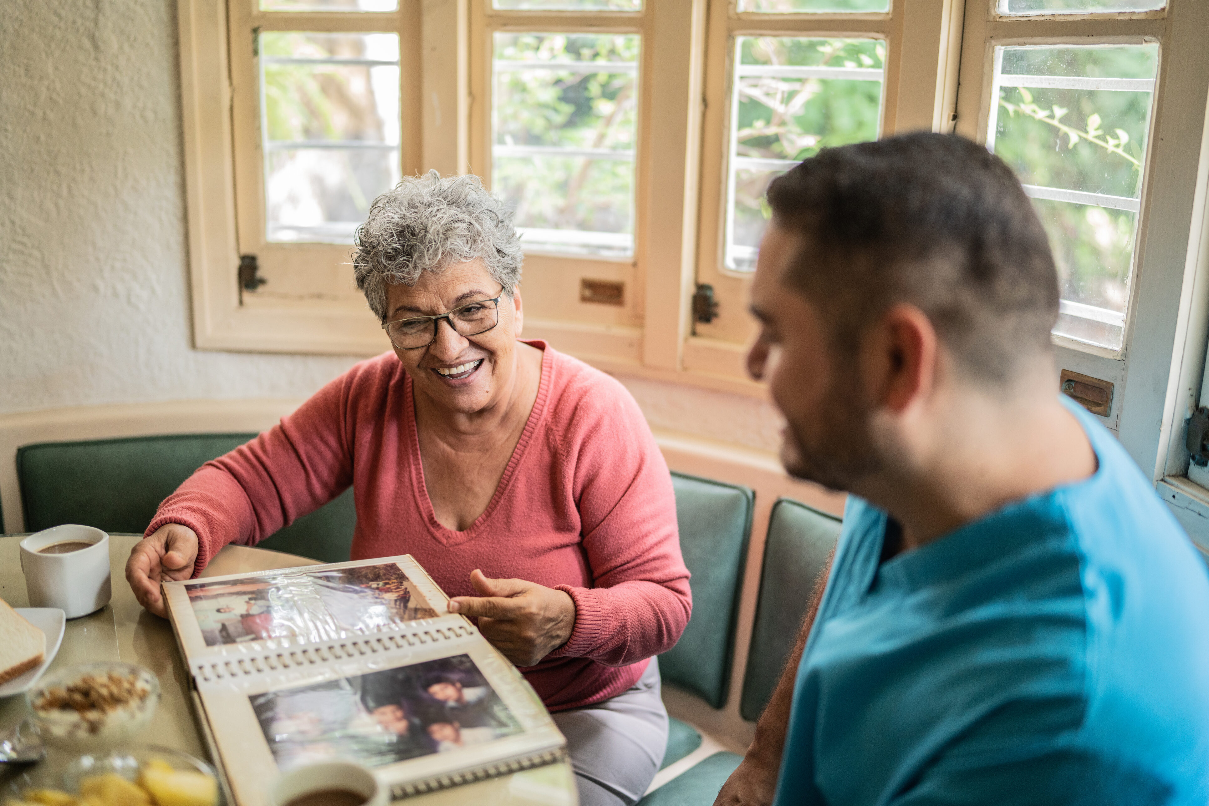 An older woman and an out-of-focus man sit at a table looking at a photo album