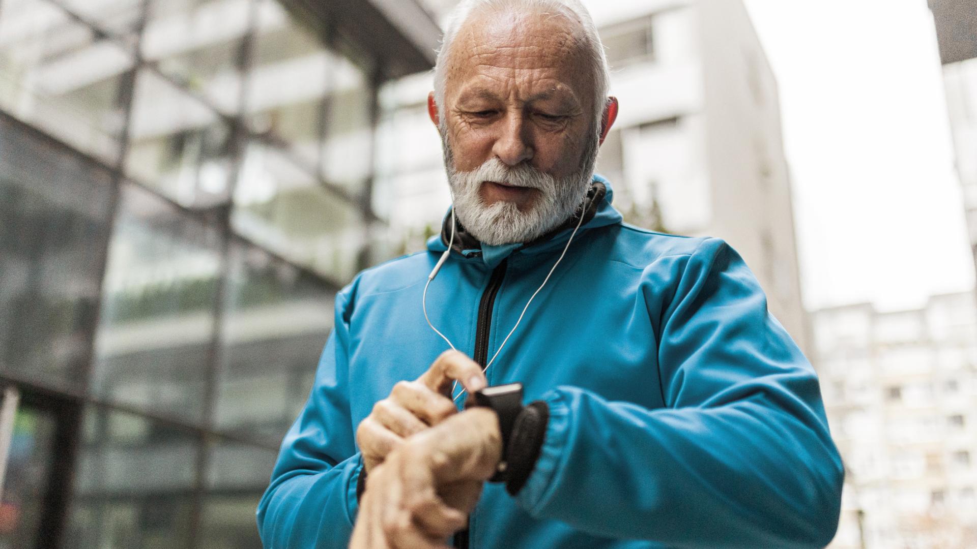 An older man in a sports jacket looks at his smart watch.