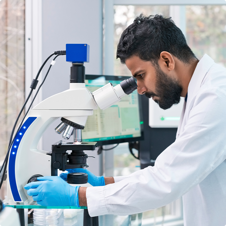 Scientist in a lab coat looking into a microscope.